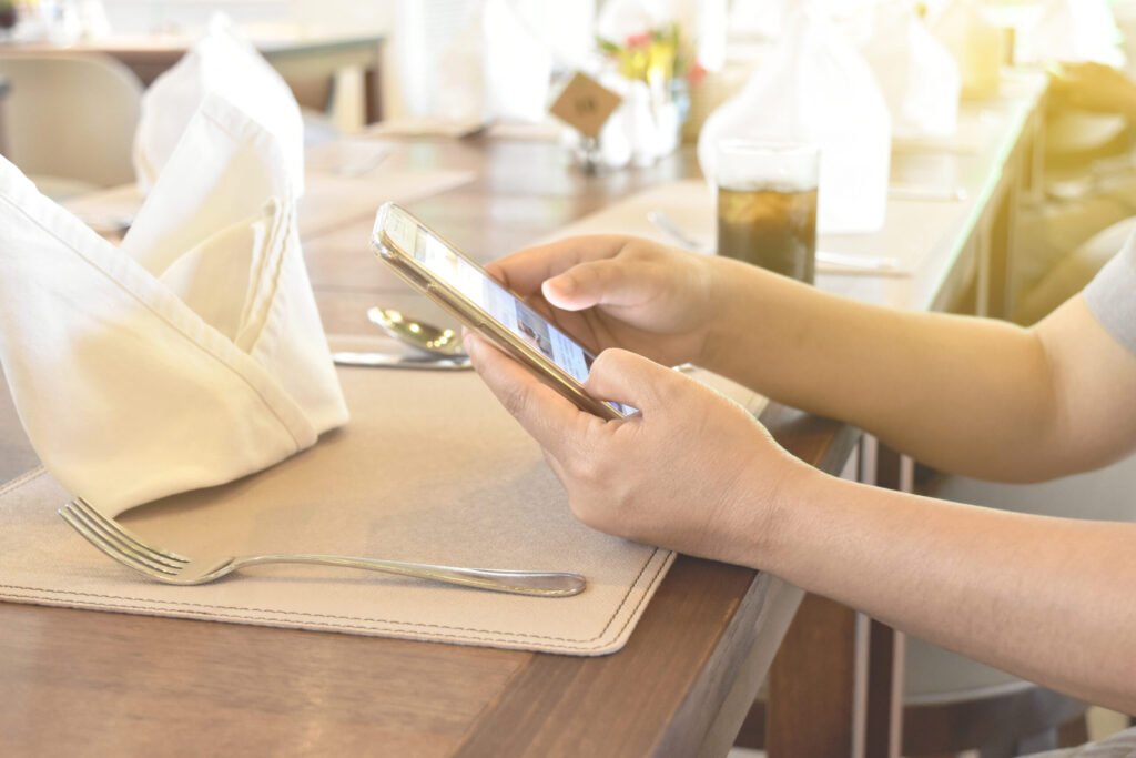 Manos de una clienta usando el móvil sobre una mesa de restaurante con servilleta y cubiertos